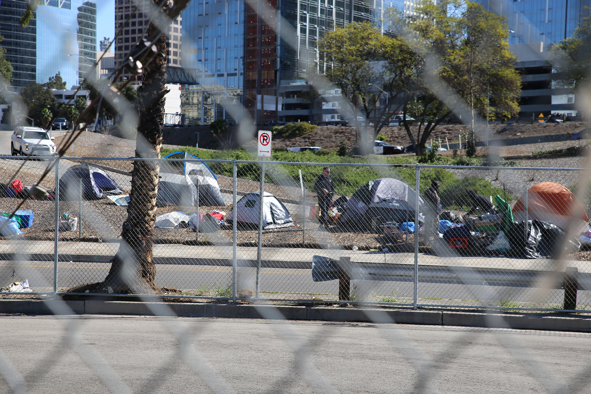 A police officer standing next to a group of tents to the side of a freeway on-ramp