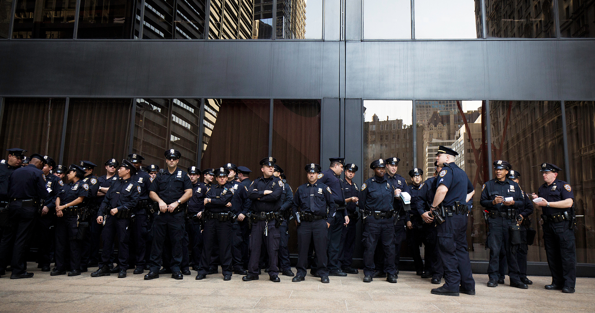 A large group of police standing together in a line in front of a high-rise building.