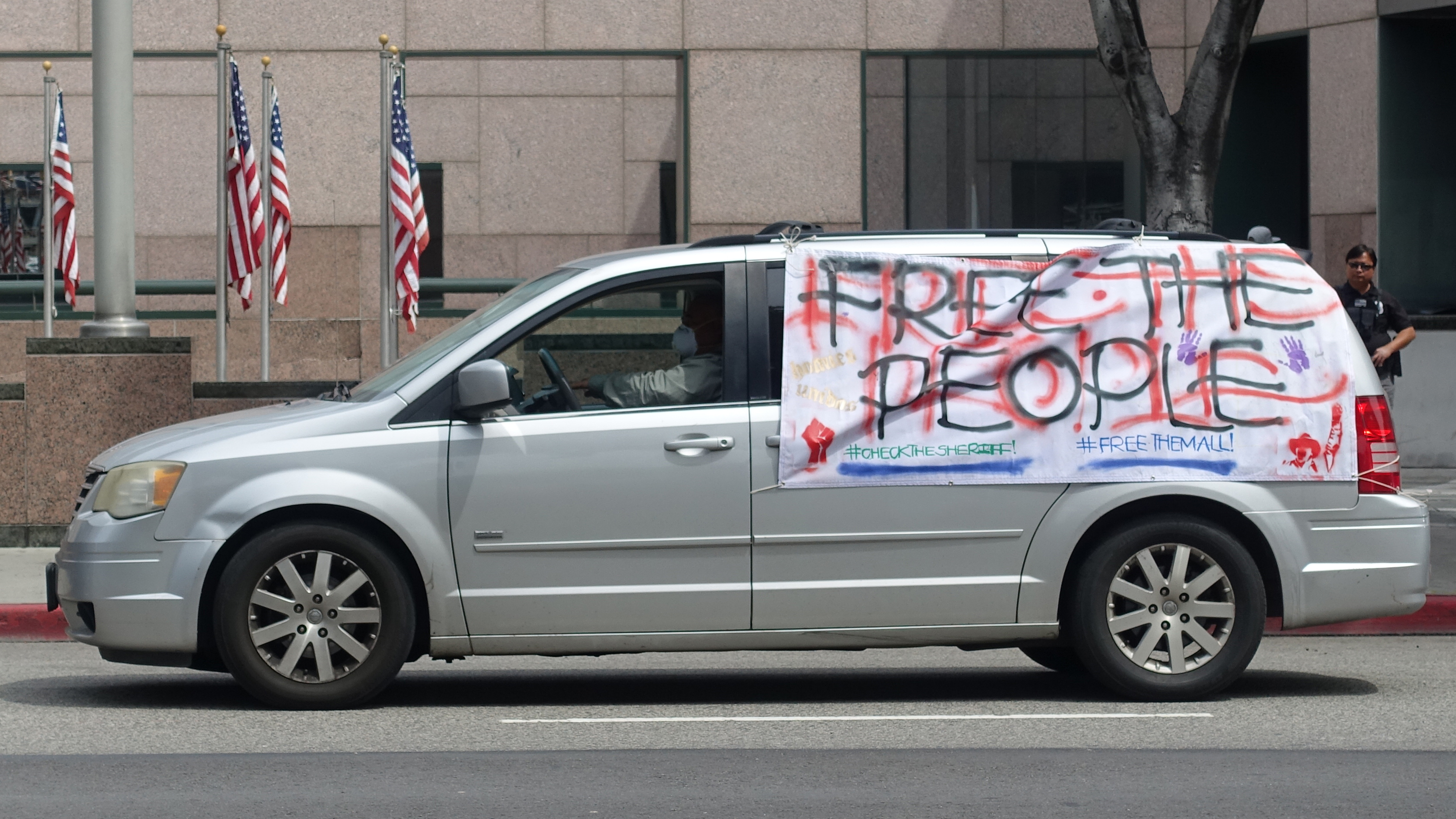 A silver van with a large hand-made sign on the side of the van that reads: Free the People, Check the Sheriff