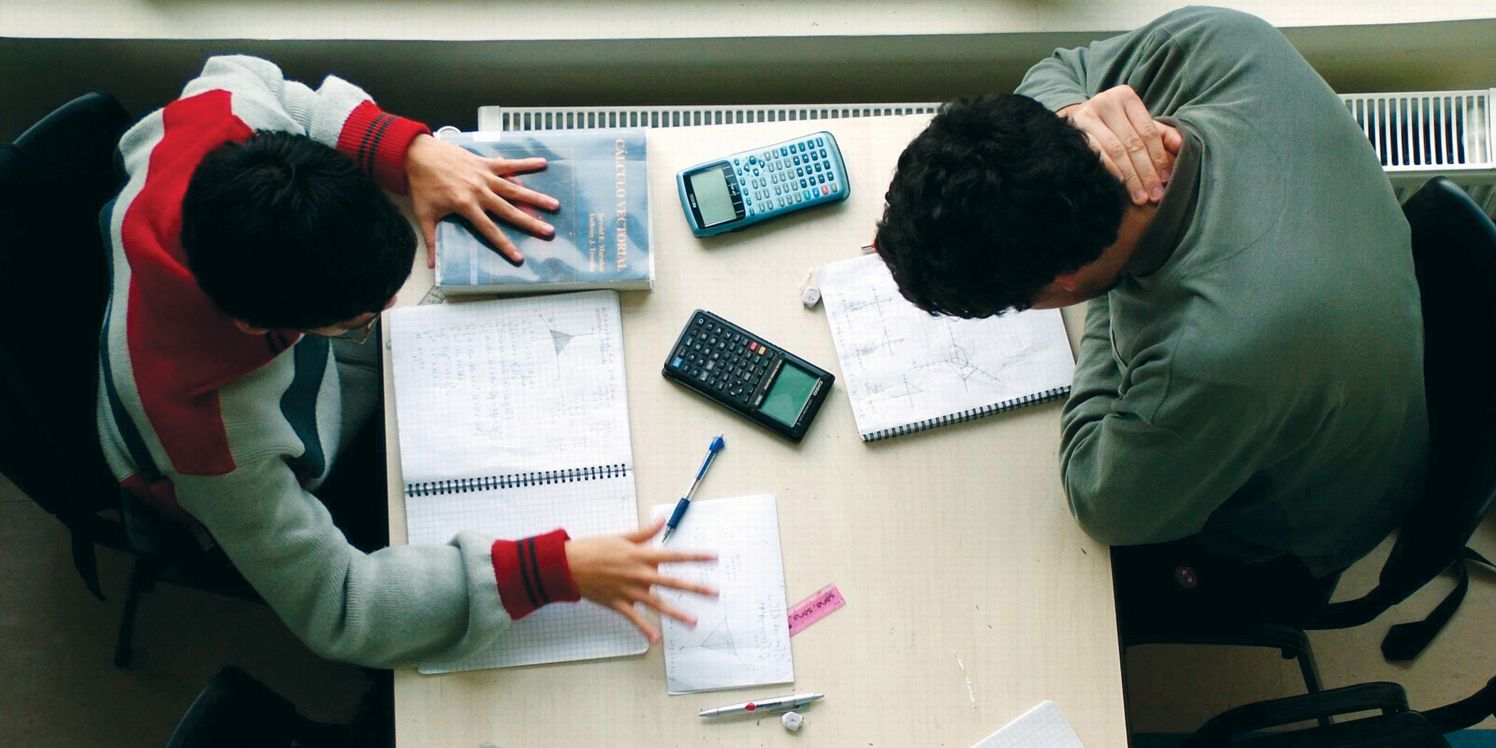 Aerial image of two people sitting on opposite sides of a table with books and calculators in front of them