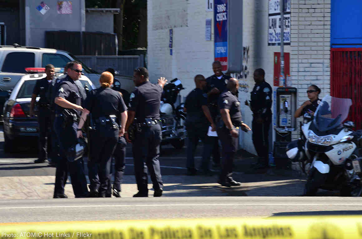 8 police officers standing on a street outside, yellow police tape in the foreground.